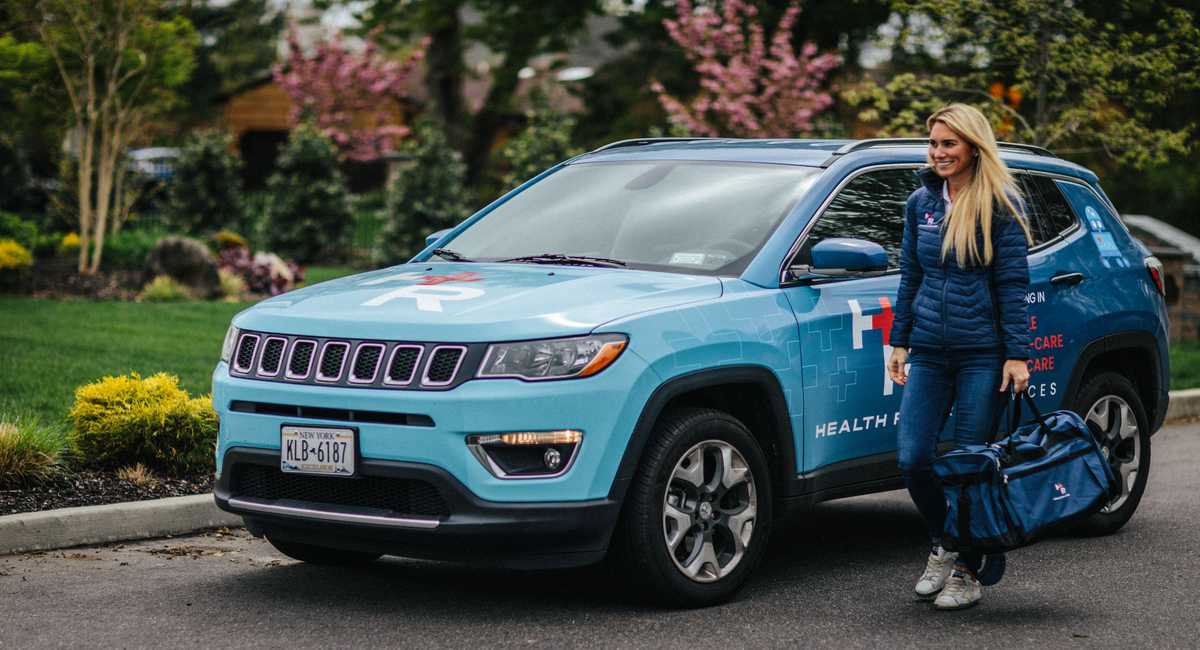 Health Rover employee standing on the left side of a Health Rover fleet vehicle, and a branded duffle bag in her left hand.